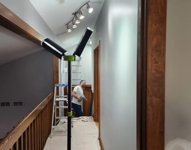 A person is painting a hallway with a ladder and lights.