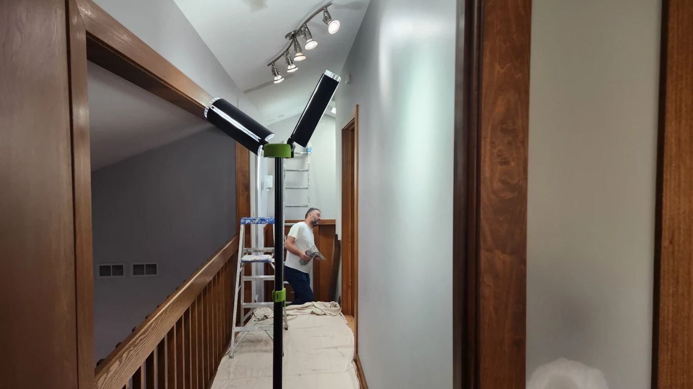 A person is painting a hallway with a ladder and lights.