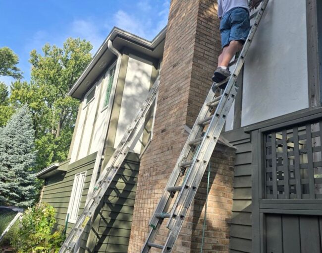 Person on ladder painting the side of a house.