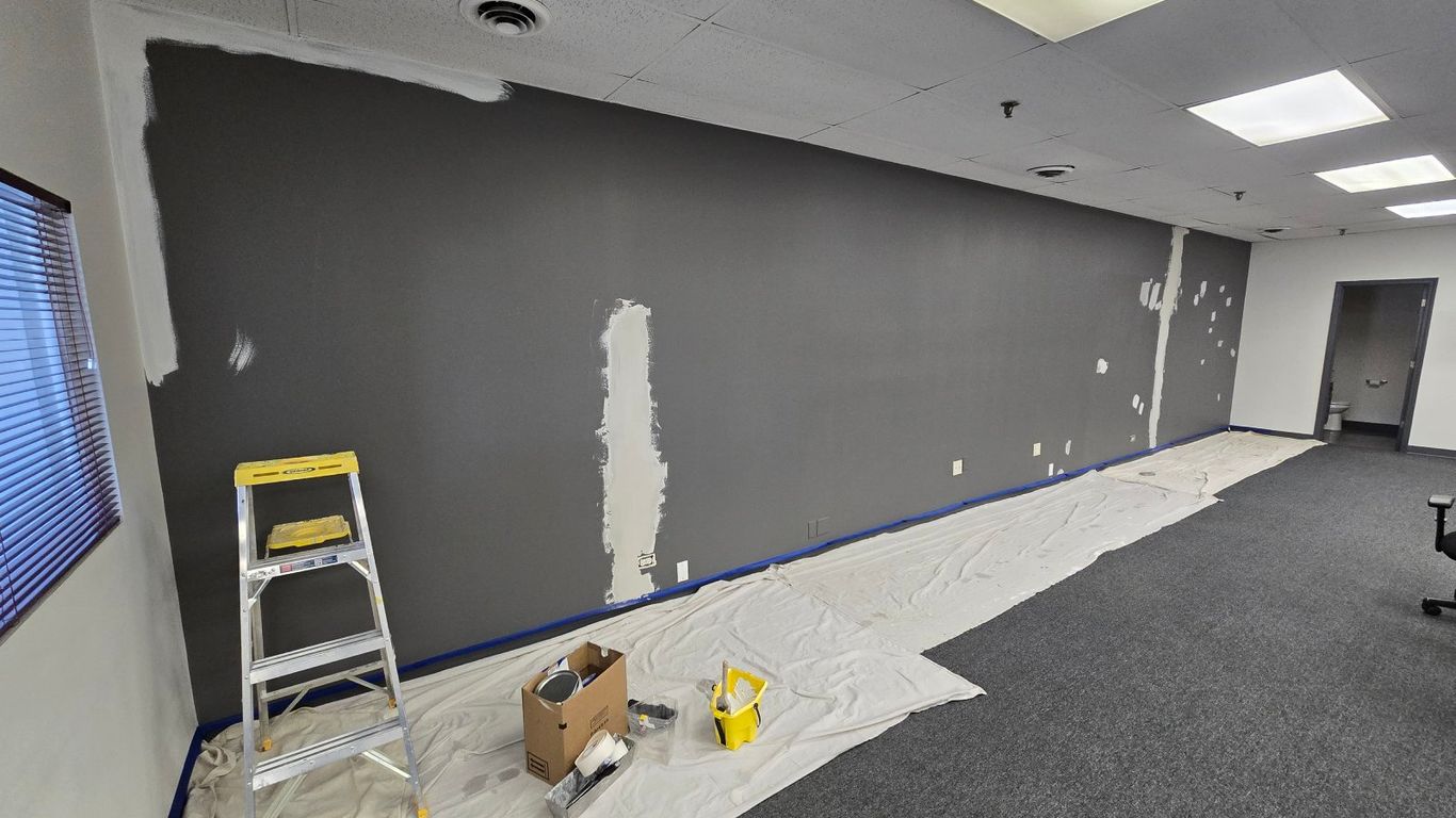 A room is being painted, with a ladder and painting supplies on drop cloths.