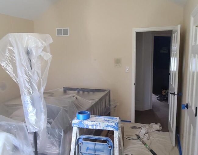 Room being painted with furniture covered in plastic.