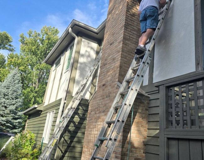 Person on ladder painting the side of a house.