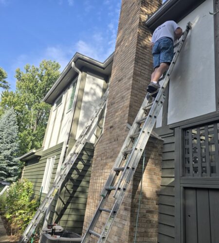A professional painter on a ladder painting a house exterior.