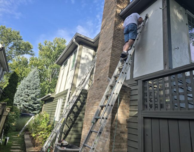 A professional painter on a ladder painting a house exterior.