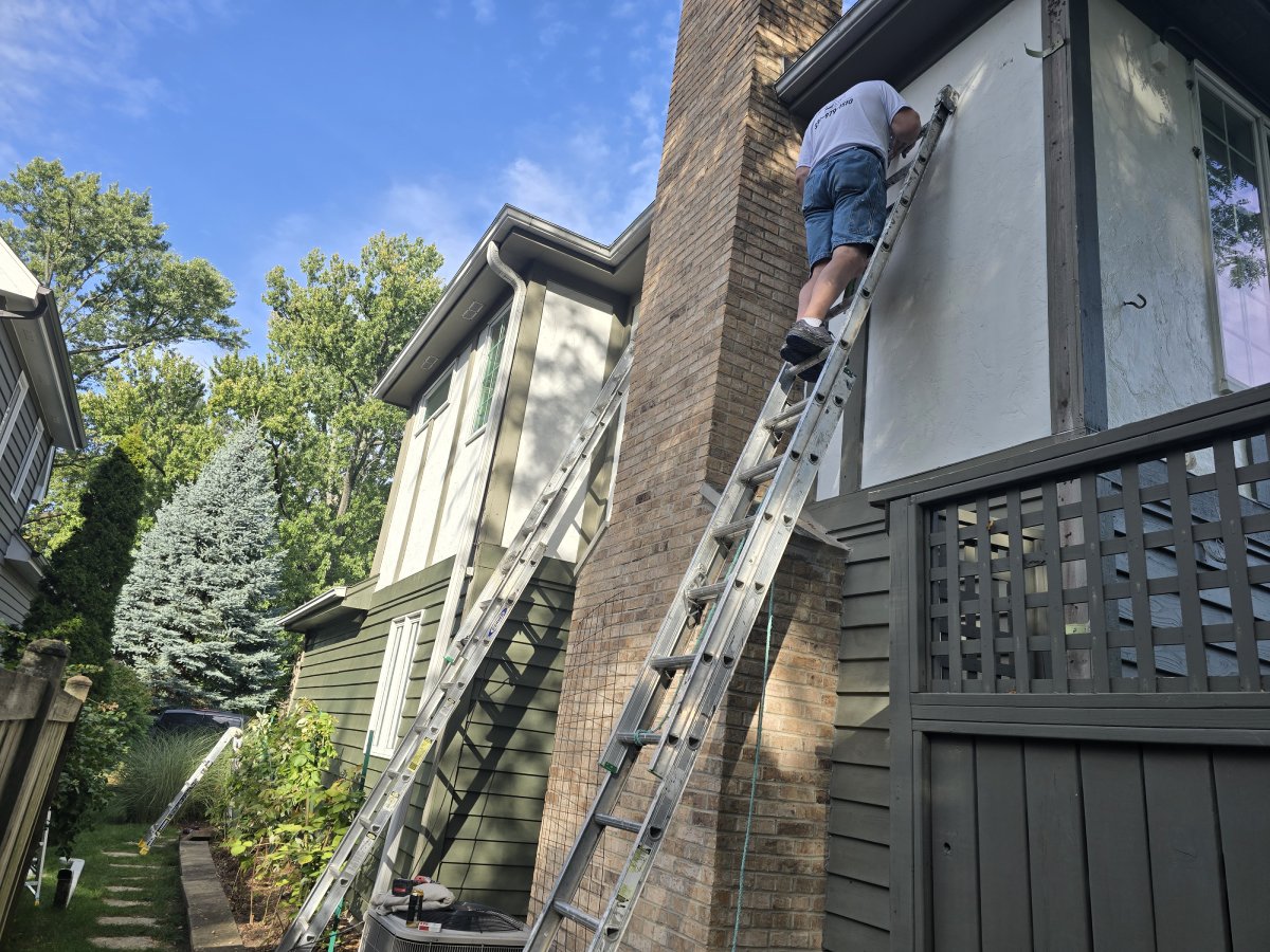 A professional painter on a ladder painting a house exterior.