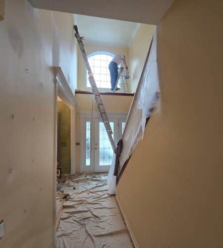 Interior hallway with a person painting on a ladder near a window reflecting a professional project.