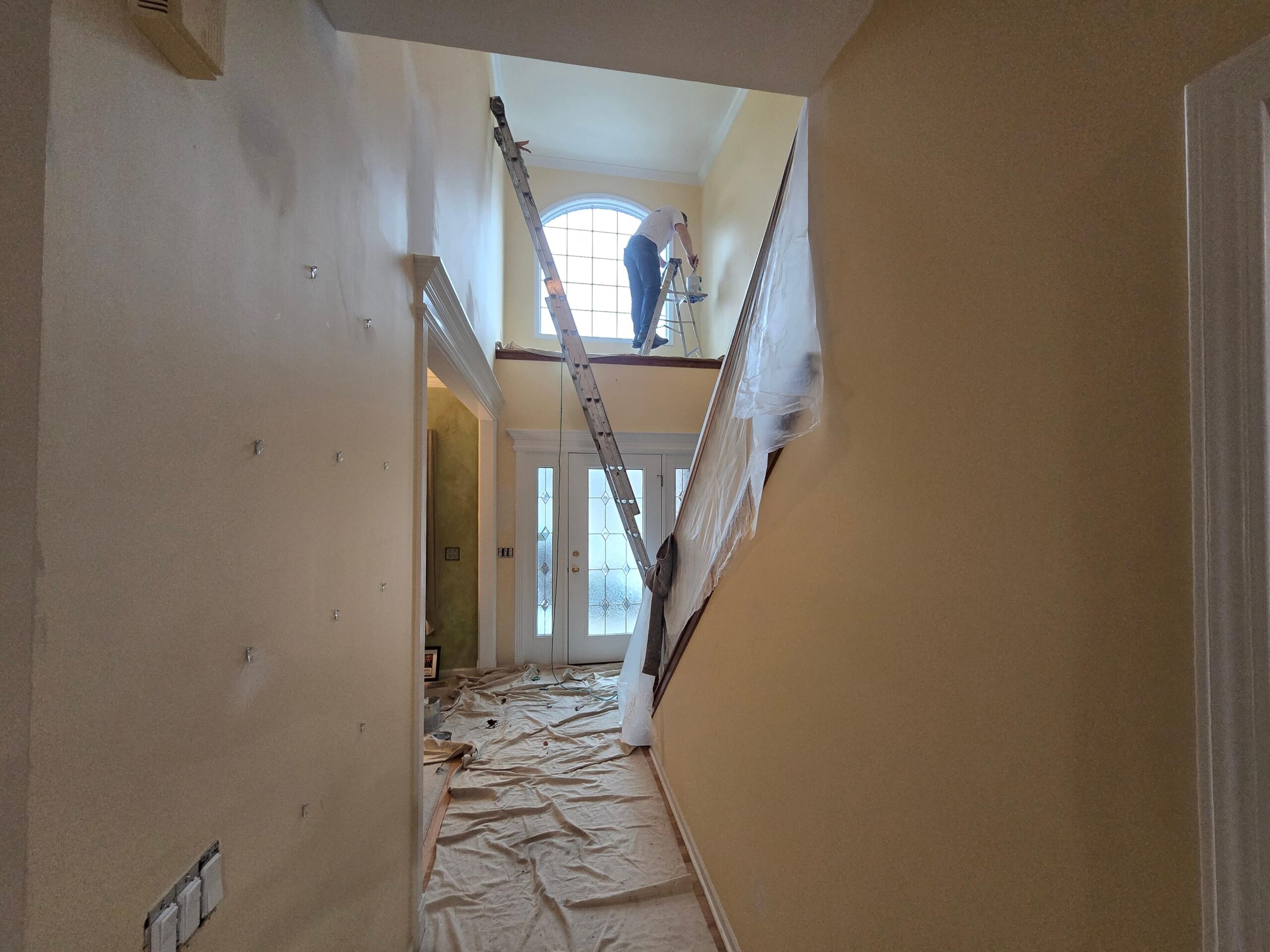 Interior hallway with a person painting on a ladder near a window reflecting a professional project.