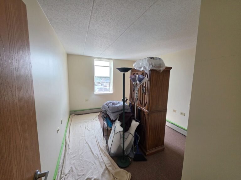 Freshly painted bedroom walls in an Elmwood Park, IL apartment, with drop cloths and masked baseboard heaters