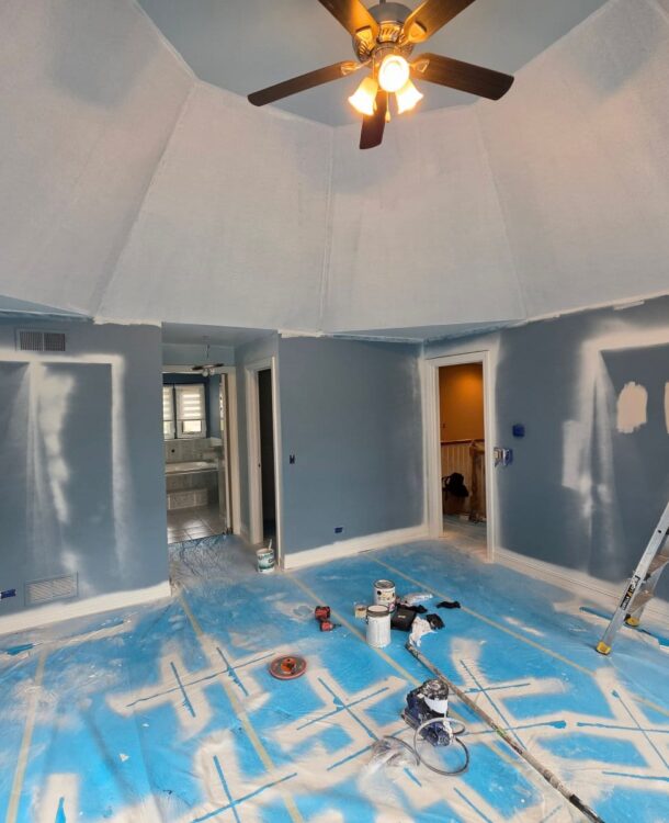 Bedroom with a vaulted ceiling being painted in Lemont, IL, with spot-primed walls and floors covered in protective plastic